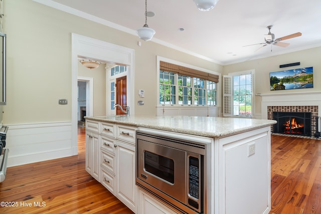 588 E Harborside Rd, Oriental, NC 28571 - kitchen with stainless steel microwave, a fireplace with flush hearth, crown molding, light wood-style floors, and light stone countertops