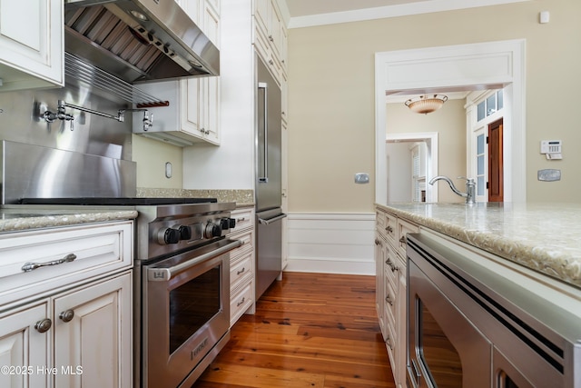 588 E Harborside Rd, Oriental, NC 28571 - kitchen with wall chimney range hood, built in appliances, dark wood-style floors, wainscoting, and light stone countertops