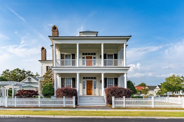 588 E Harborside Rd, Oriental, NC 28571 - neoclassical home featuring a balcony, covered porch, a chimney, and a fenced front yard