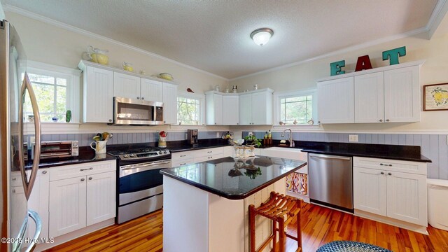 305 E New Hampshire Ave, Southern Pines, NC 28387 - kitchen with appliances with stainless steel finishes, white cabinets, light wood finished floors, a kitchen breakfast bar, and crown molding