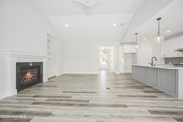 947 Ashburton Rd SE, Bolivia, NC 28422 - unfurnished living room featuring vaulted ceiling, built in shelves, recessed lighting, light wood-style floors, and a glass covered fireplace