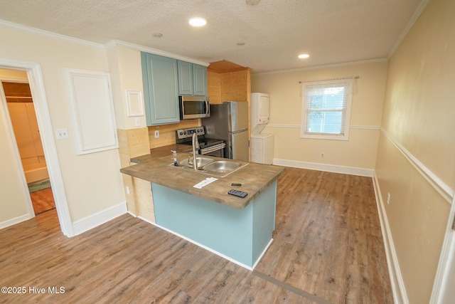 2264 New River Inlet Rd Unit 210, North Topsail Beach, NC 28460 - kitchen with appliances with stainless steel finishes, stacked washer and clothes dryer, crown molding, light wood finished floors, and a peninsula