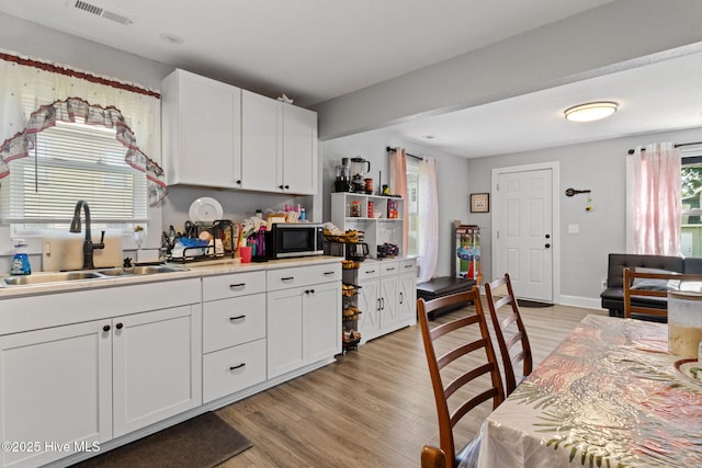 406 Walnut St, Elizabeth City, NC 27909 - kitchen featuring a sink, stainless steel microwave, white cabinetry, light wood-style floors, and light countertops