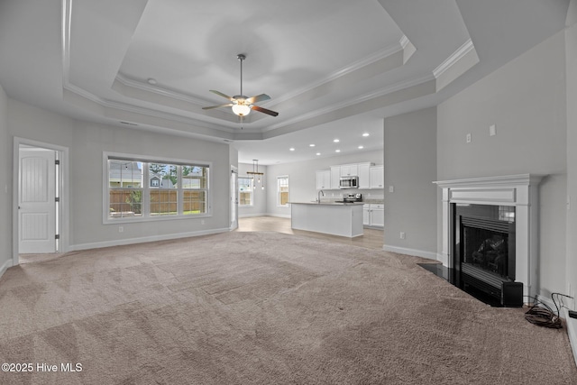 2001 Snapper St, New Bern, NC 28562 - unfurnished living room featuring light colored carpet, ceiling fan, a tray ceiling, a fireplace with flush hearth, and crown molding