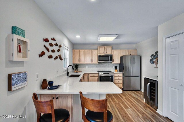 1116 E Beach Dr, Oak Island, NC 28465 - kitchen featuring stainless steel appliances, beverage cooler, light brown cabinets, a peninsula, and light wood-type flooring