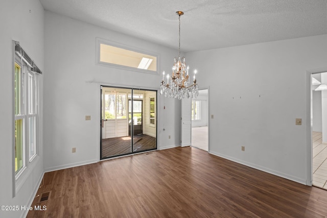 304 Lord Granville Dr, Morehead City, NC 28557 - unfurnished dining area with wood finished floors, a chandelier, a towering ceiling, baseboards, and a textured ceiling