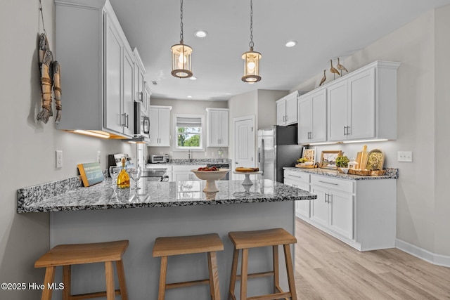 104 S 30th St, Morehead City, NC 28557 - kitchen featuring stainless steel appliances, a peninsula, a kitchen breakfast bar, stone countertops, and light wood-type flooring