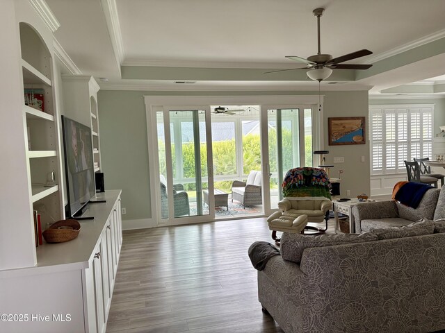 7000 Sevilleen Dr SW, Ocean Isle Beach, NC 28469 - living room featuring a ceiling fan, crown molding, a tray ceiling, and light wood-style floors