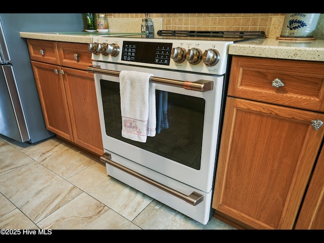 1133 Grandiflora Dr, Leland, NC 28451 - kitchen with electric stove, freestanding refrigerator, brown cabinets, and light tile patterned floors