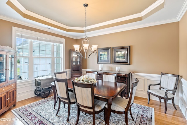3059 Irwin Dr SE, Southport, NC 28461 - dining space featuring a raised ceiling, a chandelier, light wood finished floors, ornamental molding, and a wainscoted wall
