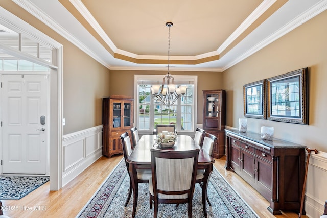 3059 Irwin Dr SE, Southport, NC 28461 - dining space featuring a tray ceiling, light wood-style floors, a chandelier, a decorative wall, and ornamental molding