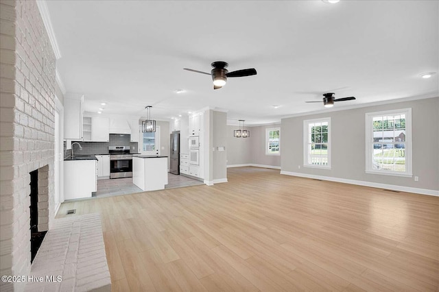 3417 Chalmers Dr, Wilmington, NC 28409 - unfurnished living room featuring a ceiling fan, baseboards, crown molding, light wood-type flooring, and a sink
