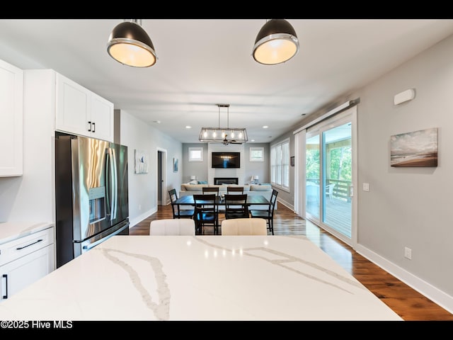 119 NE 27th St, Oak Island, NC 28465 - kitchen with stainless steel fridge with ice dispenser, open floor plan, dark wood finished floors, white cabinets, and decorative light fixtures