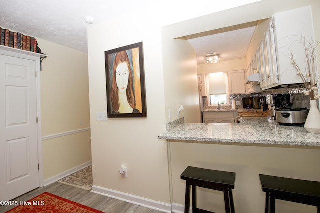 940 Linden Rd Unit 19, Pinehurst, NC 28374 - kitchen featuring wood finished floors, a breakfast bar, baseboards, a peninsula, and a textured ceiling
