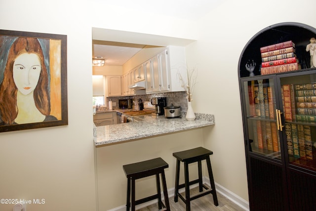 940 Linden Rd Unit 19, Pinehurst, NC 28374 - kitchen with under cabinet range hood, stainless steel range oven, backsplash, light wood-style flooring, and a breakfast bar