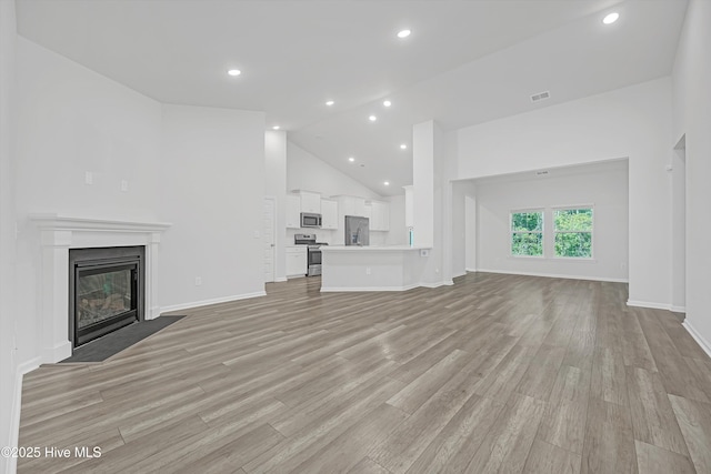 6437 Twinspur Ct SW, Ocean Isle Beach, NC 28469 - unfurnished living room featuring high vaulted ceiling, recessed lighting, light wood-type flooring, and a fireplace with flush hearth