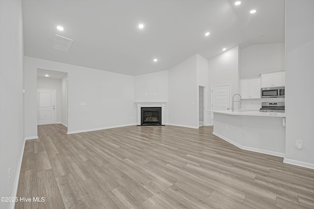 6437 Twinspur Ct SW, Ocean Isle Beach, NC 28469 - unfurnished living room featuring light wood-style floors, recessed lighting, a fireplace with flush hearth, and high vaulted ceiling