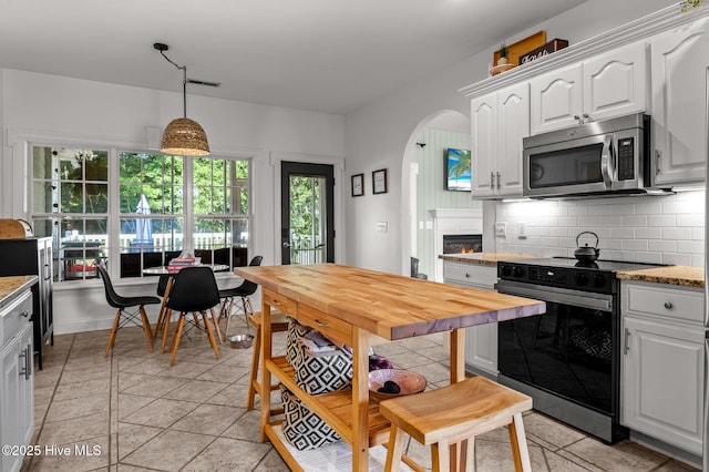 1682 Gores Landing Rd SW, Ocean Isle Beach, NC 28469 - kitchen with stainless steel microwave, black electric range, white cabinetry, tasteful backsplash, and arched walkways