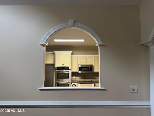 315 Hunters Creek Dr, Goldsboro, NC 27534 - kitchen with appliances with stainless steel finishes, arched walkways, backsplash, cream cabinetry, and crown molding