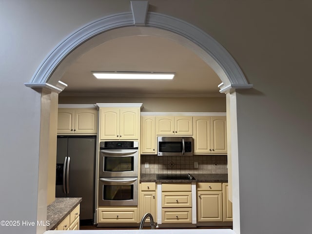 315 Hunters Creek Dr, Goldsboro, NC 27534 - kitchen featuring stainless steel appliances, cream cabinetry, arched walkways, decorative columns, and dark countertops