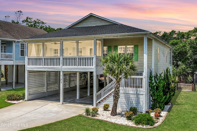409 Womble St, Oak Island, NC 28465 - beach home with concrete driveway, a carport, a sunroom, a shingled roof, and a ceiling fan