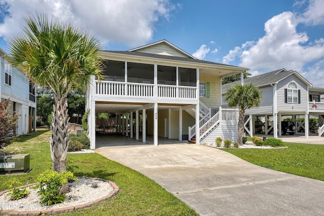 409 Womble St, Oak Island, NC 28465 - raised beach house with a carport, driveway, a sunroom, a shingled roof, and a front lawn