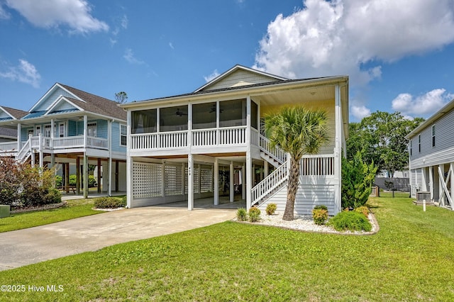 409 Womble St, Oak Island, NC 28465 - back of property featuring stairs, concrete driveway, a carport, a sunroom, and a lawn