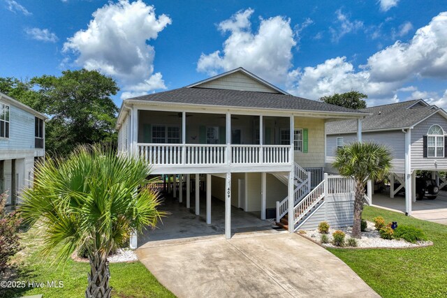 409 Womble St, Oak Island, NC 28465 - raised beach house featuring a carport, driveway, a sunroom, ceiling fan, and roof with shingles