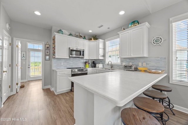 3725 Island Dr, North Topsail Beach, NC 28460 - kitchen with stainless steel appliances, a peninsula, white cabinetry, a breakfast bar area, and recessed lighting