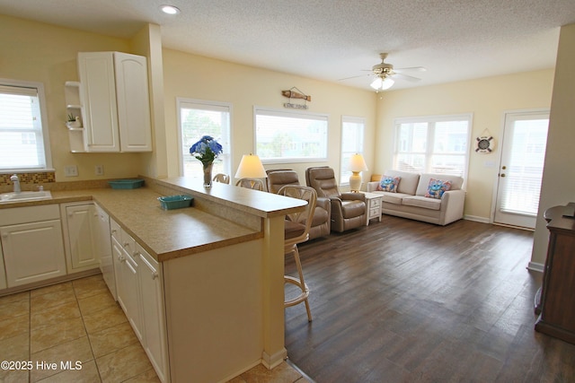 405 27th St Unit A, Sunset Beach, NC 28468 - kitchen featuring a breakfast bar area, a sink, a peninsula, a ceiling fan, and white cabinetry