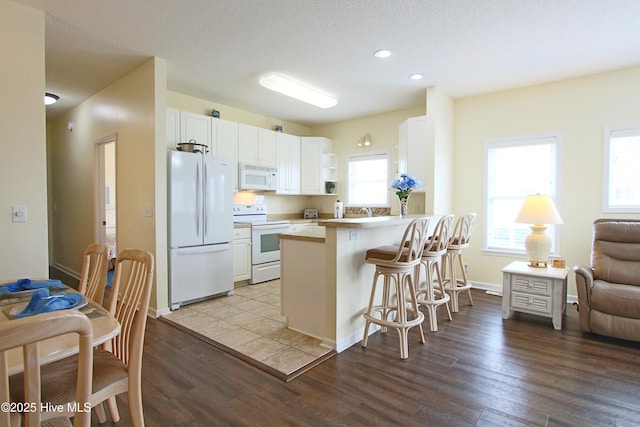 405 27th St Unit A, Sunset Beach, NC 28468 - kitchen featuring white appliances, white cabinets, a kitchen breakfast bar, wood finished floors, and a peninsula