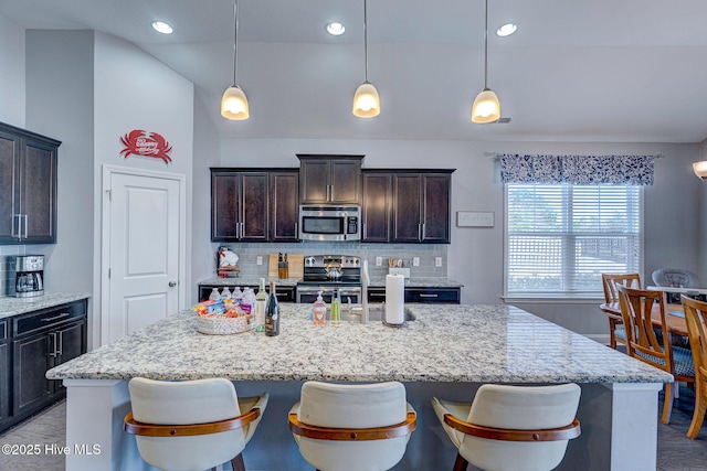 576 Steele Loop, Wilmington, NC 28411 - kitchen featuring appliances with stainless steel finishes, tasteful backsplash, an island with sink, light stone countertops, and lofted ceiling