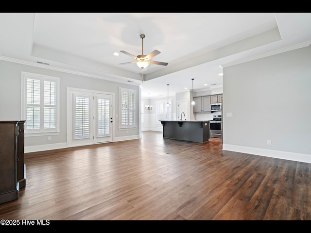 7024 Bonaventure St SW, Ocean Isle Beach, NC 28469 - unfurnished living room featuring a tray ceiling, ceiling fan, dark wood finished floors, crown molding, and a chandelier