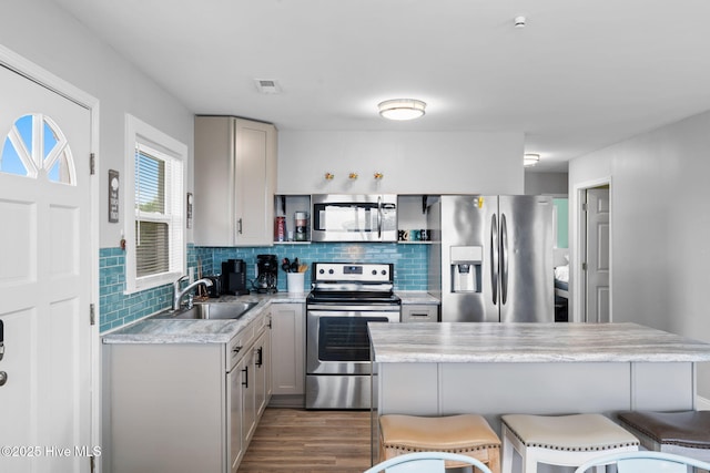 926 E Beach Dr, Oak Island, NC 28465 - kitchen featuring appliances with stainless steel finishes, a sink, a kitchen bar, decorative backsplash, and wood finished floors