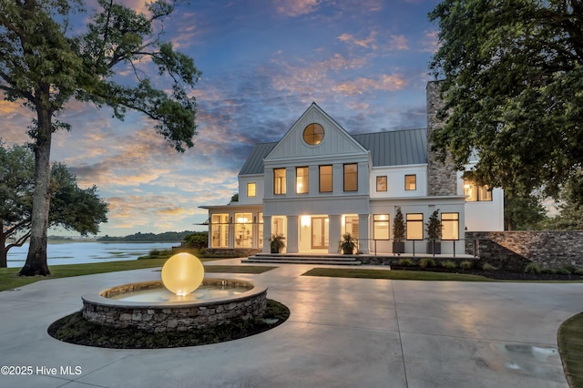 1064 Ocean Ridge Dr, Wilmington, NC 28405 - back of property at dusk featuring a standing seam roof, curved driveway, a water view, metal roof, and stucco siding