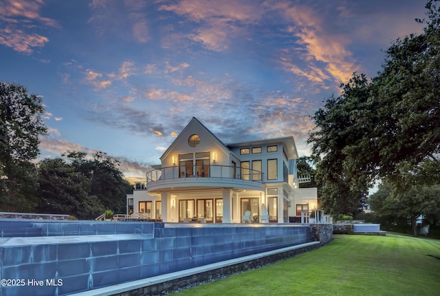 1064 Ocean Ridge Dr, Wilmington, NC 28405 - back of property at dusk featuring a balcony, a lawn, a pool, and stucco siding