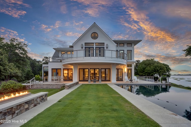 1064 Ocean Ridge Dr, Wilmington, NC 28405 - back of house at dusk featuring a balcony, a yard, a patio area, an outdoor fire pit, and stucco siding