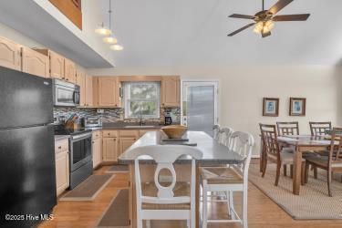 6707 Kings Lynn Dr, Oak Island, NC 28465 - kitchen featuring stainless steel appliances, light brown cabinetry, ceiling fan, backsplash, and lofted ceiling