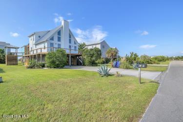 6707 Kings Lynn Dr, Oak Island, NC 28465 - view of green lawn with concrete driveway, a carport, and stairway