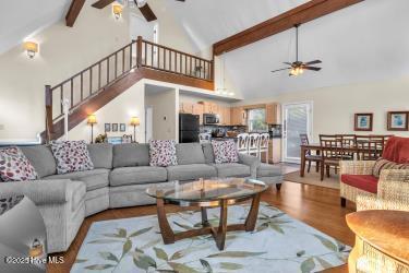 6707 Kings Lynn Dr, Oak Island, NC 28465 - living area featuring a ceiling fan, beam ceiling, high vaulted ceiling, wood finished floors, and stairway