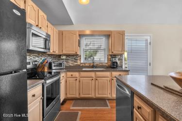6707 Kings Lynn Dr, Oak Island, NC 28465 - kitchen featuring stainless steel appliances, light brown cabinetry, a sink, wood finished floors, and decorative backsplash