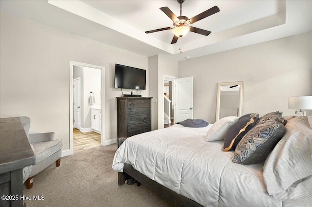 5735 Orchardgrass Rd, Leland, NC 28451 - bedroom with a tray ceiling, light colored carpet, baseboards, ensuite bath, and ceiling fan