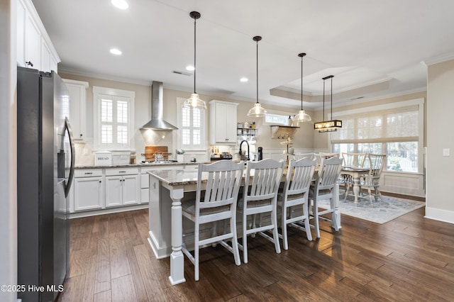 3020 Eno Ln, Leland, NC 28451 - kitchen with stainless steel fridge, wall chimney exhaust hood, ornamental molding, white cabinets, and light stone counters