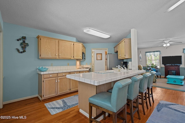 109 NE 1st St, Oak Island, NC 28465 - kitchen with tile countertops, a ceiling fan, a kitchen bar, freestanding refrigerator, and light wood-style floors