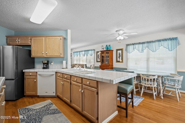109 NE 1st St, Oak Island, NC 28465 - kitchen featuring dishwasher, freestanding refrigerator, a peninsula, light wood-style floors, and tile countertops