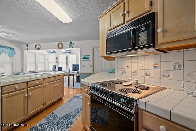 109 NE 1st St, Oak Island, NC 28465 - kitchen featuring black appliances, tile countertops, a textured ceiling, a ceiling fan, and light wood-style flooring