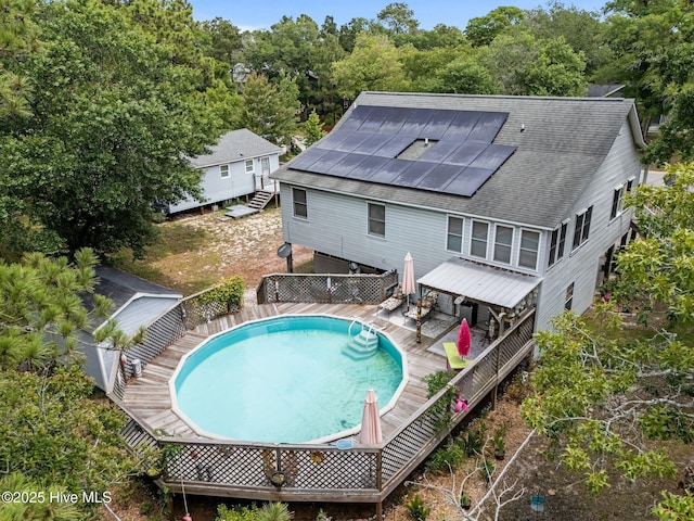109 NE 1st St, Oak Island, NC 28465 - rear view of house with solar panels, a deck, an outdoor pool, and roof with shingles