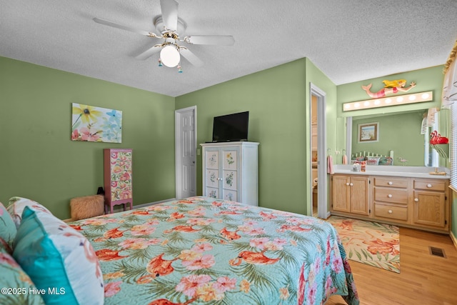 109 NE 1st St, Oak Island, NC 28465 - bedroom with light wood-style floors, a textured ceiling, ceiling fan, and ensuite bath