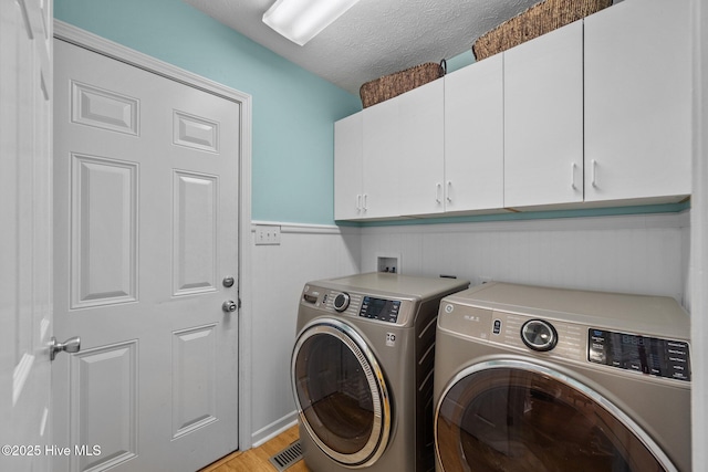 206 Lansing Ct, Jacksonville, NC 28540 - laundry room with cabinet space, washer and clothes dryer, light wood finished floors, a textured ceiling, and a wainscoted wall