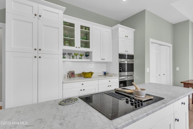 2021 Seawind Ln, Wilmington, NC 28405 - kitchen featuring stainless steel double oven, black electric cooktop, backsplash, white cabinetry, and light stone countertops